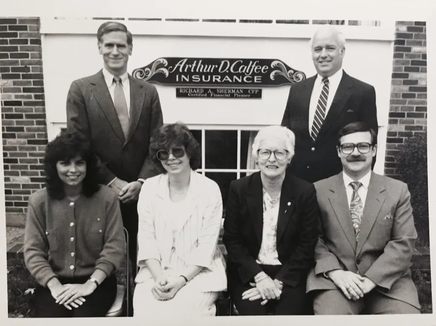 The Calfee Insurance team in front of the agency sign, black and white archive photo